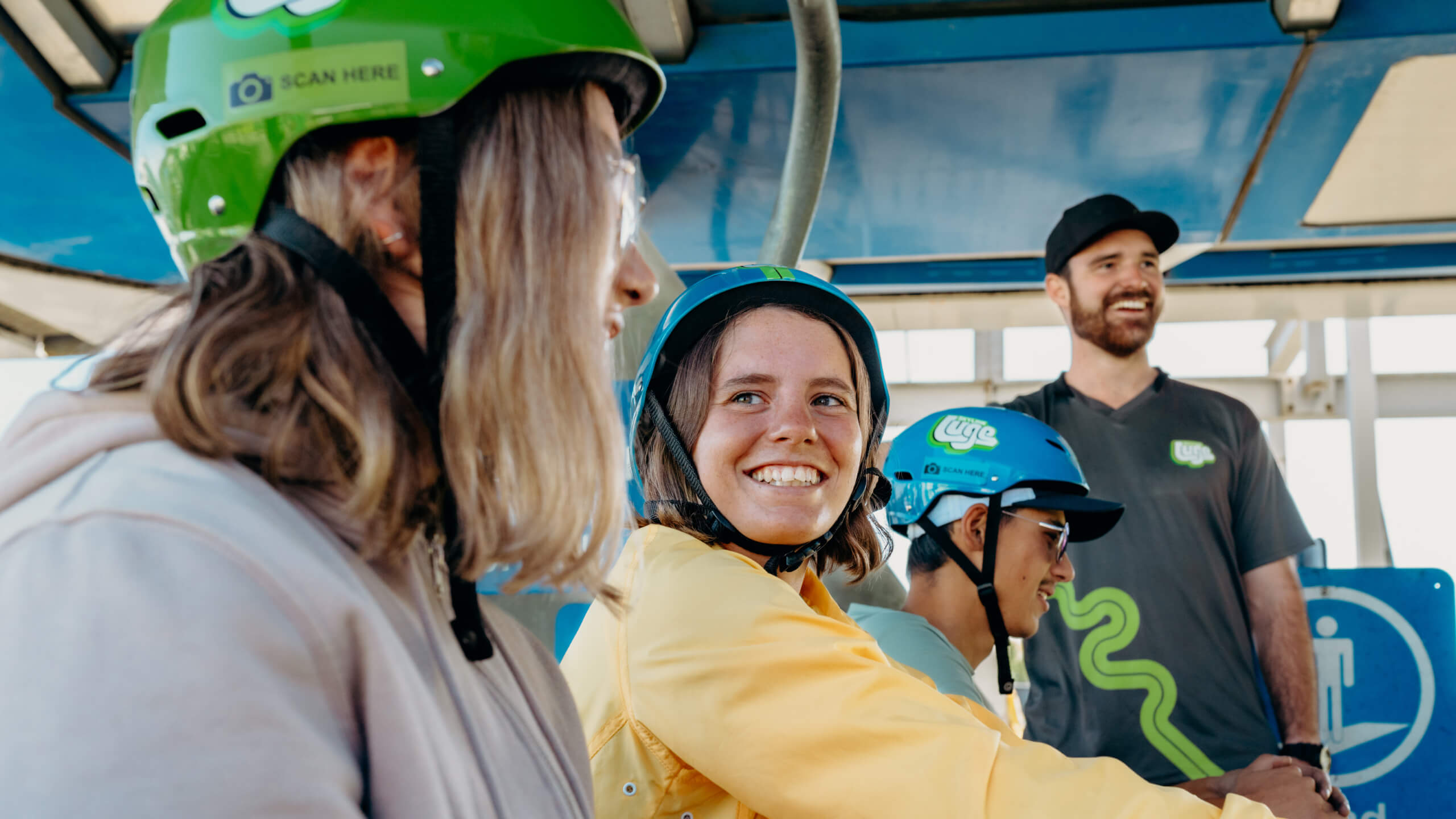 A group of friends smiling in luge helmets as they anticipate a ride on the luge